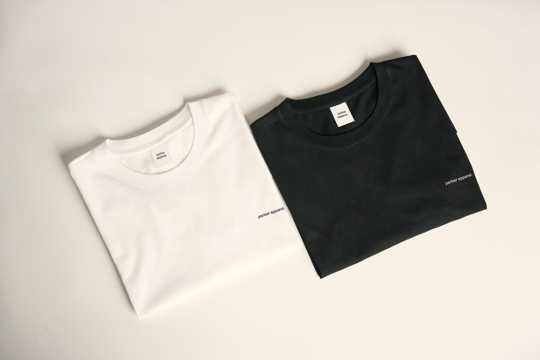 Two folded Parker Apparel tees, one white and one black, each printed with the lowercase parker apparel wordmark